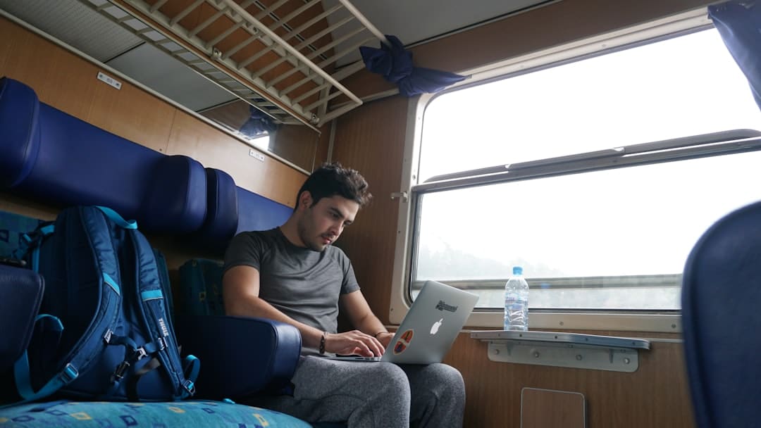 Man seated on a train using a laptop by the window.